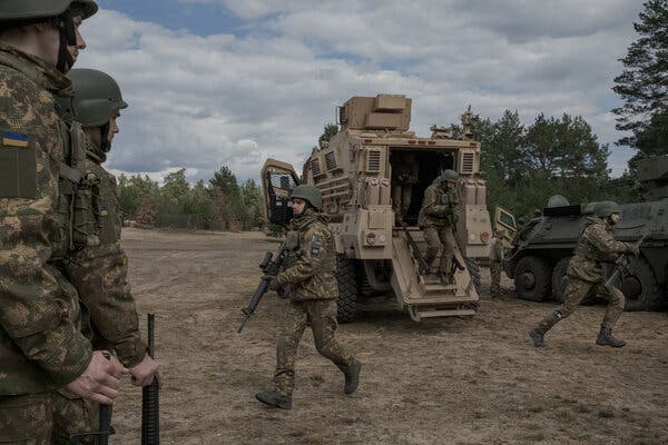 Soldiers with guns emerging from a troop carrier.