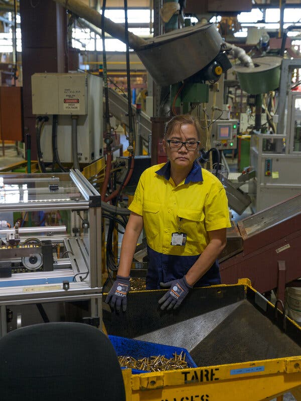 A worker in a yellow shirt stands in a factory and next to a bin that is receiving cartridges.